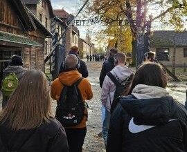 Fotografie mit jungen Menschen vor dem Eingang zu einer Gedenkstätte in Deutschland mit Gebäuden und Baumbestand.